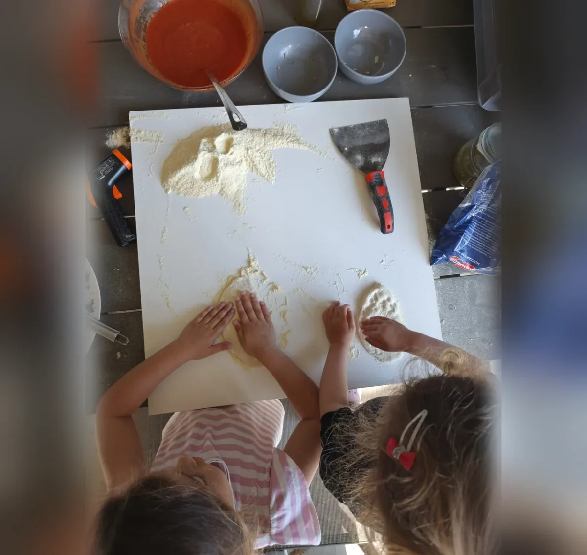 Twee kinderen die zelf pizzadeeg uitduwen op een met bloem bestoven plank