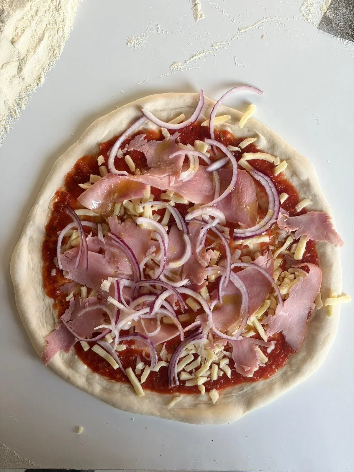 Een pizza met ham en rode ui, klaar voor de oven