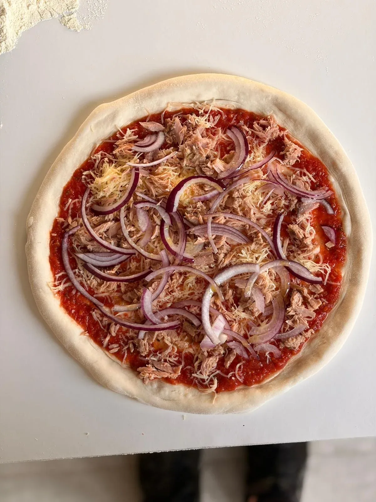 Een pizza met tonijn en rode ui, klaar voor de oven